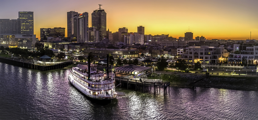 New Orleans travel guide image of a Mississippi River riverboat with the downtown skyline at sunset